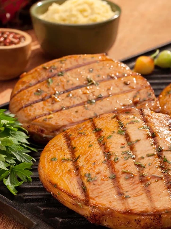 Foto de produto da Frimesa, mostrando bistecas suínas grelhadas e temperadas.