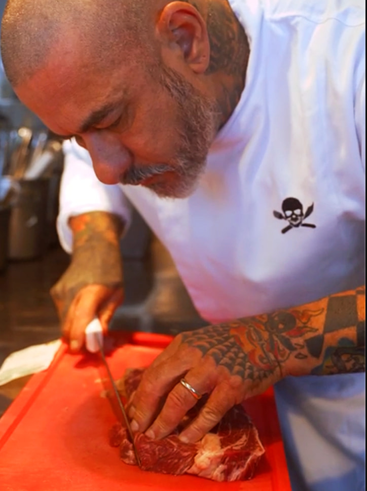O chef Henrique Fogaça cortando um bife de carne em uma tábua vermelha, em uma imagem para a campanha da Go Planet que conecta gastronomia e sustentabilidade.