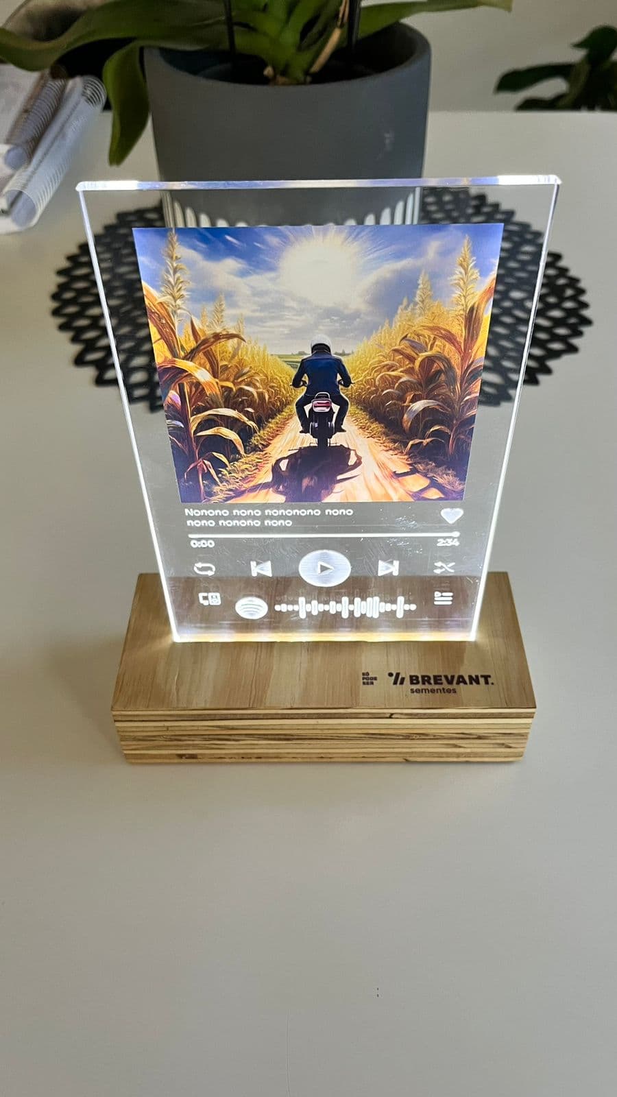 Luminária de acrílico personalizada no formato de uma tela do Spotify, com o logo da Brevant Sementes na base de madeira.